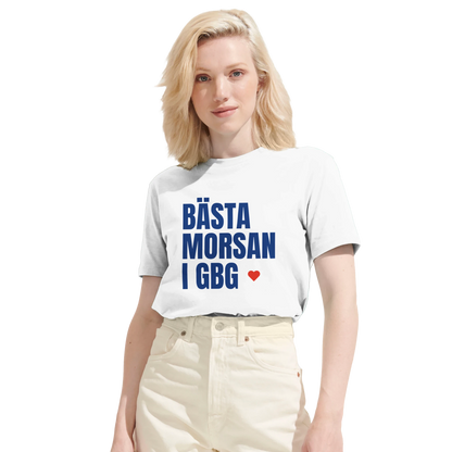 Kvinna bär en vit 'Bästa morsan i GBG' t-shirt. Bilden visar tröjans runda halsringning och tydliga brösttryck.