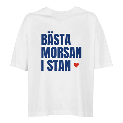 Vit oversized t-shirt i ekologisk bomull med texten 'Bästa morsan i stan' och ett litet rött hjärta. En stilren och hållbar present till mamma.