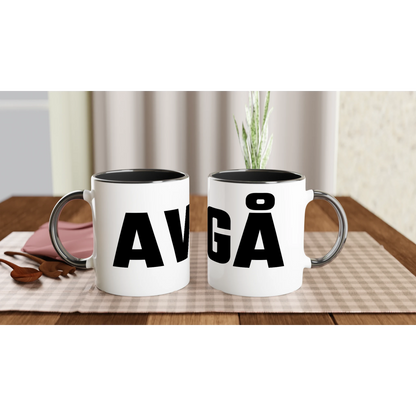 En miljöbild med två vita muggar på ett dukat bord. Muggarna har svart insida och handtag, och trycken visar 'AV' och 'GÅ', vilket tillsammans bildar motivet 'AVGÅ'.