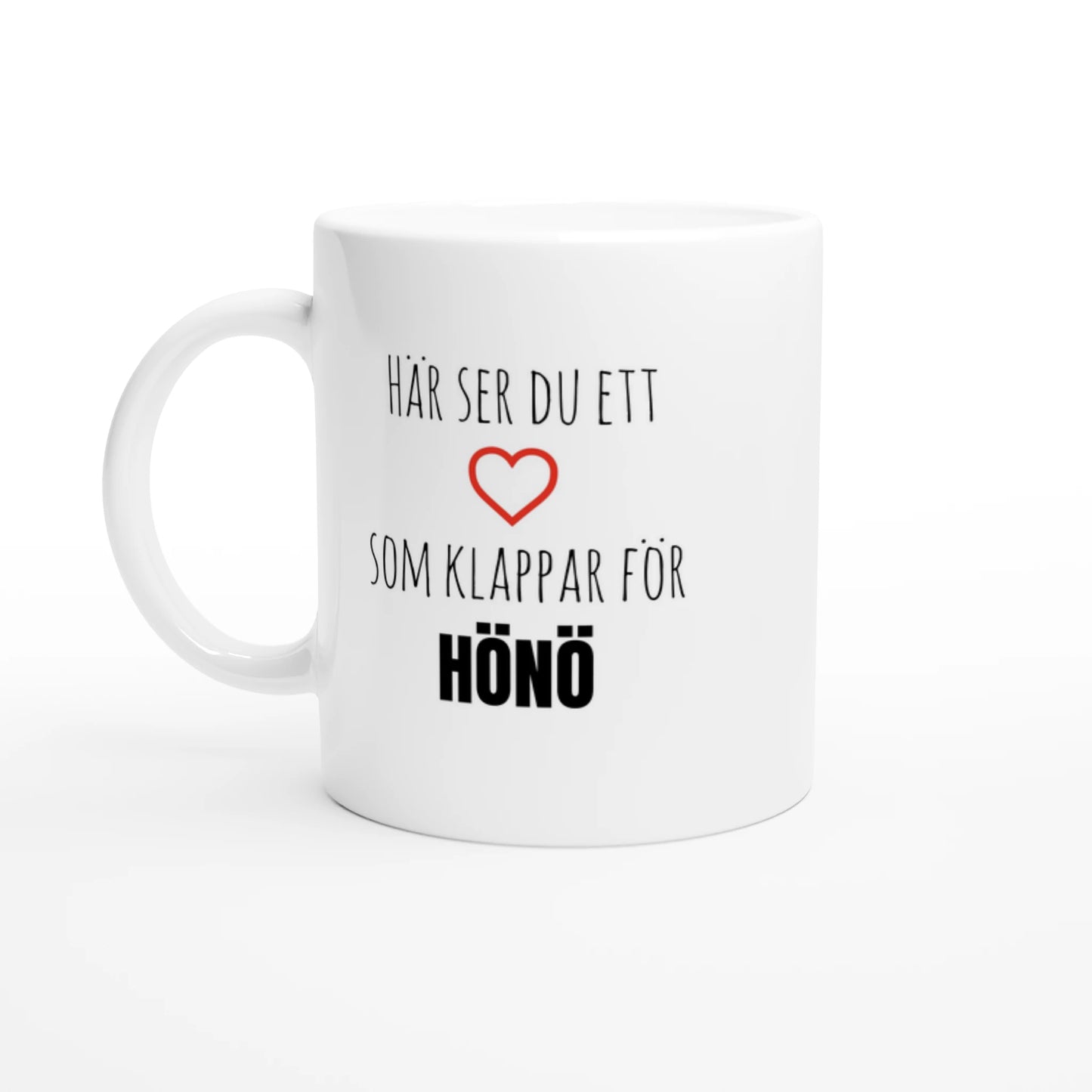 Vit kaffemugg med texten 'Här ser du ett hjärta som klappar för Hönö' och ett rött hjärta. En stilren mugg för alla som älskar Hönö i Göteborgs norra skärgård.