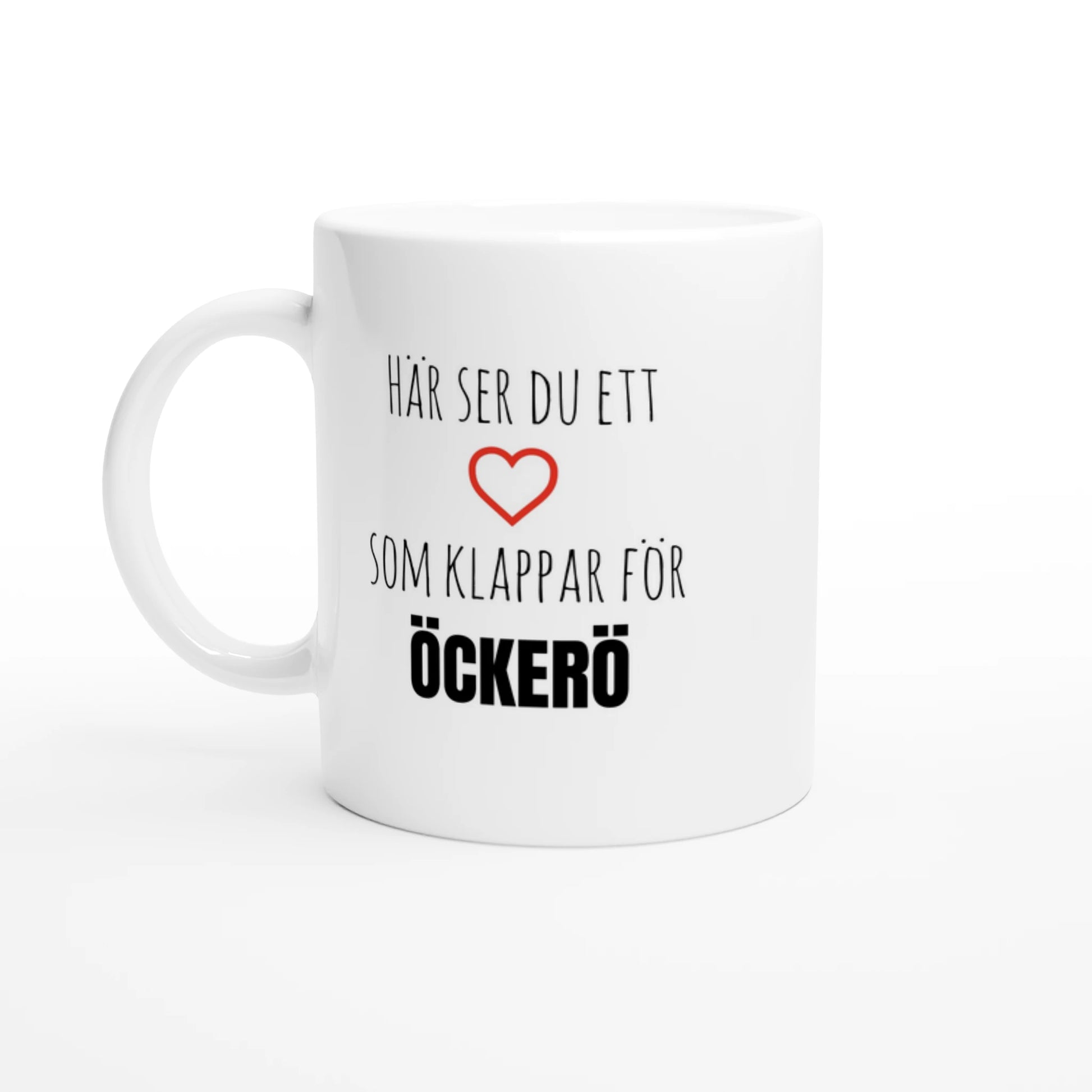 Vit keramisk mugg med texten 'Här ser du ett hjärta som klappar för Öckerö' och ett rött hjärta. En fin kaffekopp för alla som älskar Öckerö.
