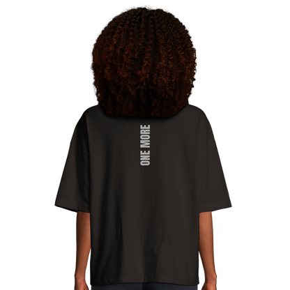 Kvinna sedd bakifrån i en svart oversized boxy tee. Visar det vertikala ryggtrycket och den trendiga passformen.