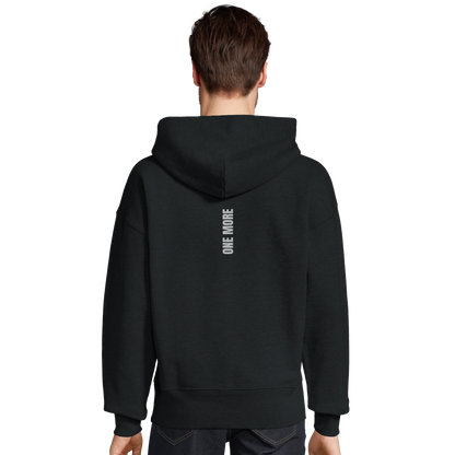 Man sedd bakifrån i en svart oversized hoodie. Visar den atletiska passformen och det vertikala trycket längs ryggen.