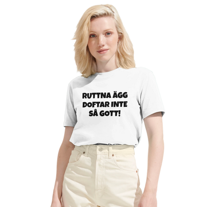 Kvinna bär en vit t-shirt med texten 'Ruttna ägg doftar inte så gott'. Visar den moderna passformen på denna roliga tröja.