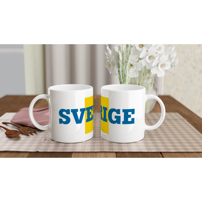 Två Sverige-muggar uppställda på ett bord för en svensk fika. Visar muggarnas design i en hemtrevlig miljö.