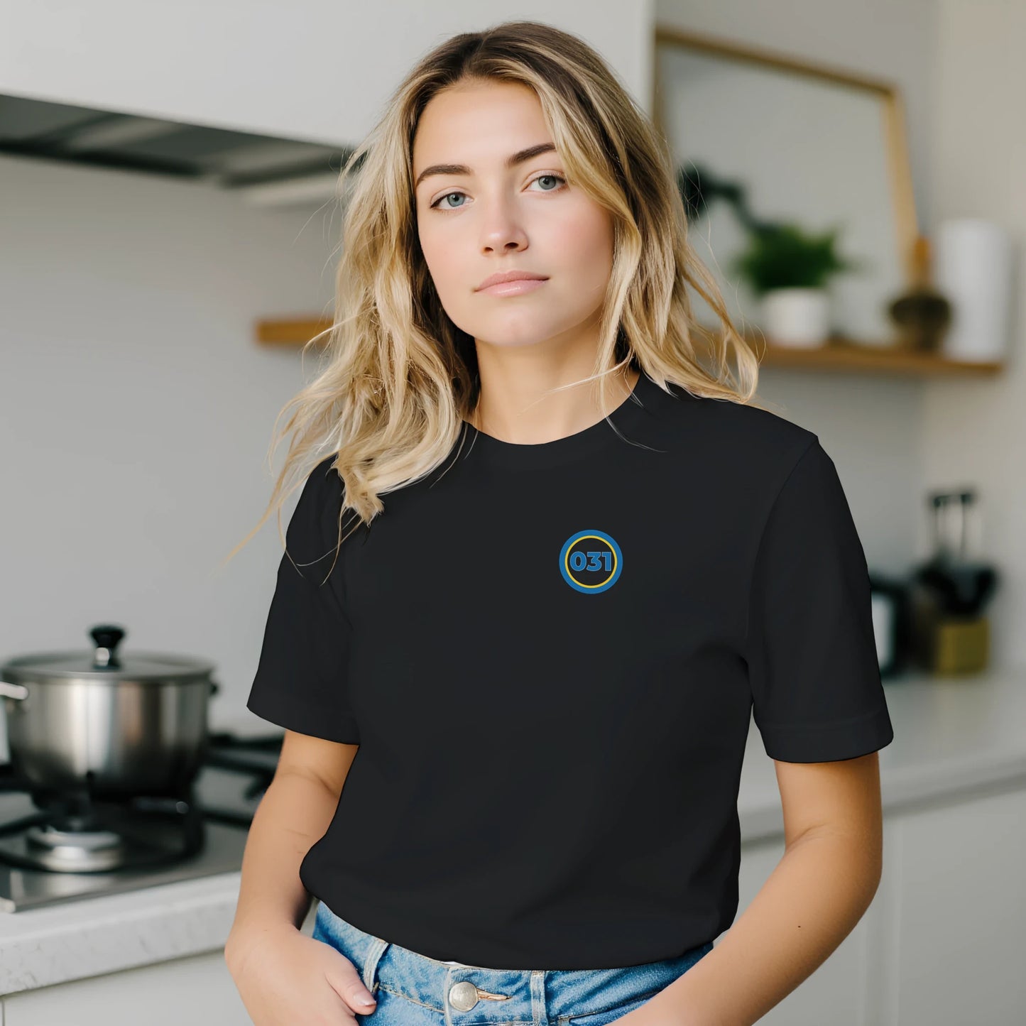 Kvinna ståendes i kök med svart t-shirt från GBGMotiv. 031 syns över vänstra bröstet.