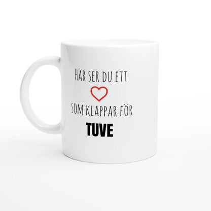 Vit kaffemugg med texten 'Här ser du ett hjärta som klappar för Tuve' och ett rött hjärta. En stilren mugg för alla som älskar Tuve på Hisingen.