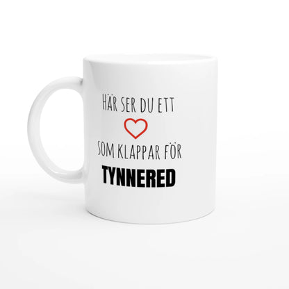 Vit kaffemugg med texten 'Här ser du ett hjärta som klappar för Tynnered' och ett rött hjärta. En stilren mugg för alla som älskar Tynnered i Västra Göteborg.